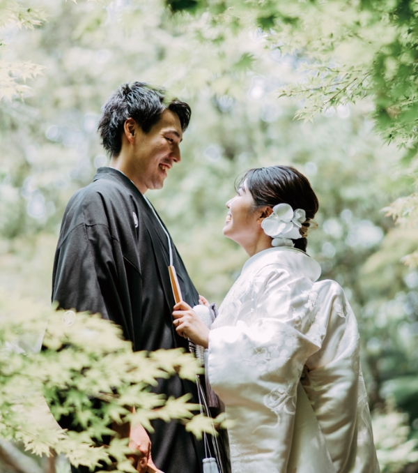 緑に囲まれた屋外で和装の新郎新婦が見つめ合い微笑む幸せな瞬間