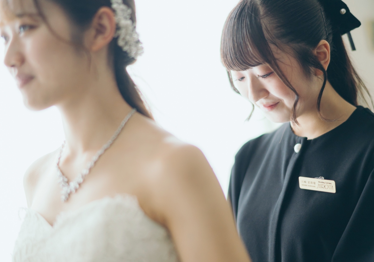 ウェディングドレス姿の花嫁の背後で、スタッフが優しく微笑んでいる場面