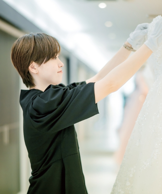 スタッフが白いドレスを手に取り調整している様子を捉えた写真